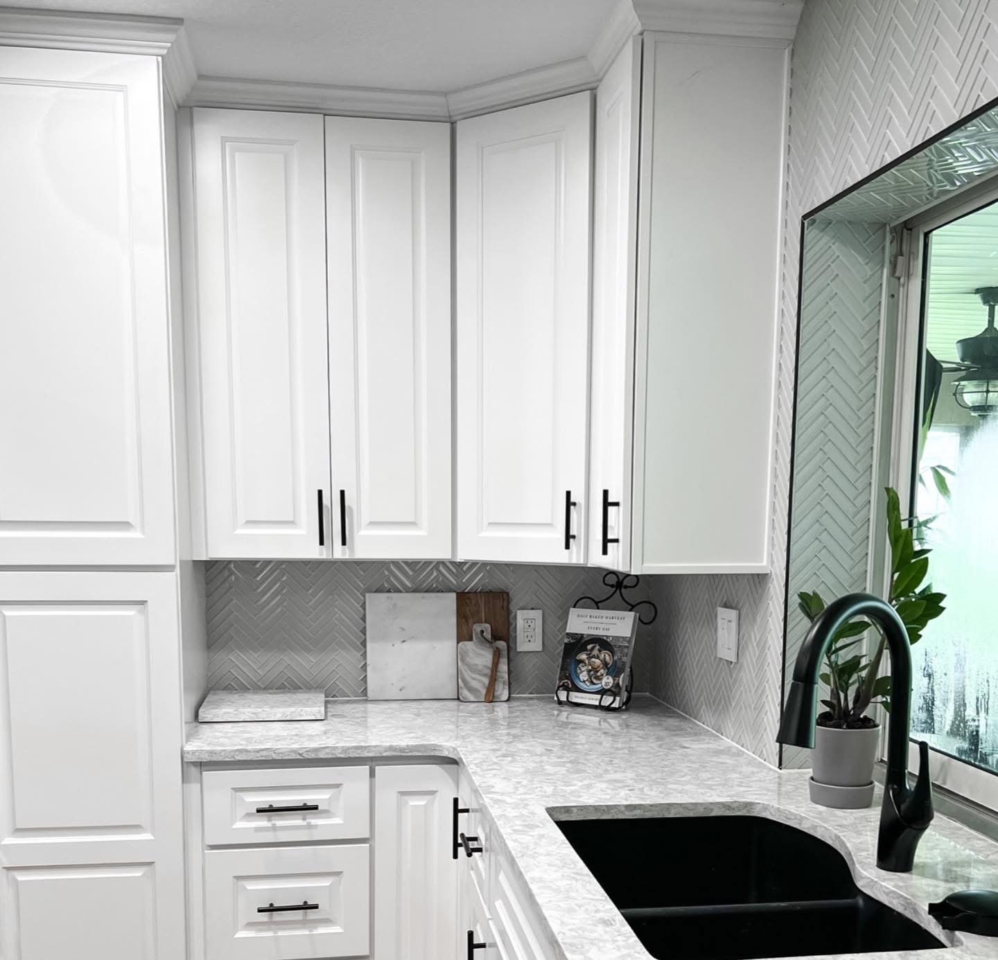 Kitchen remodel detail — white shaker cabinets, herringbone tile backsplash, quartz countertop, matte black hardware